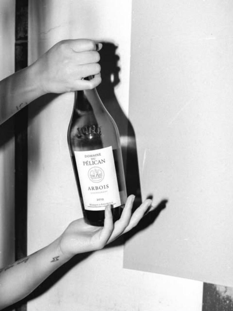 Hand holding a bottle of Domaine du Pélican against a wall