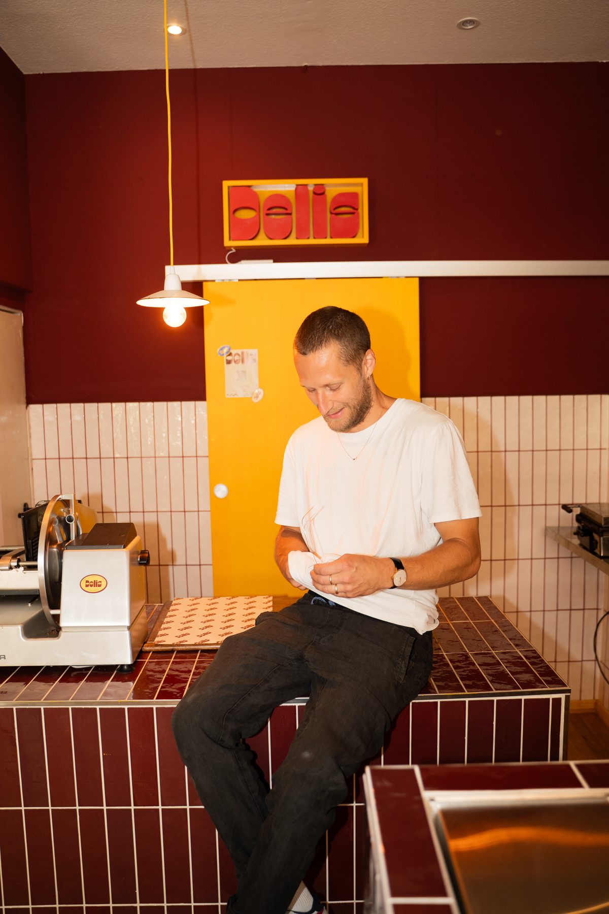Marco, the founder, sitting on the burgundy tiled counter under the DELIS sign