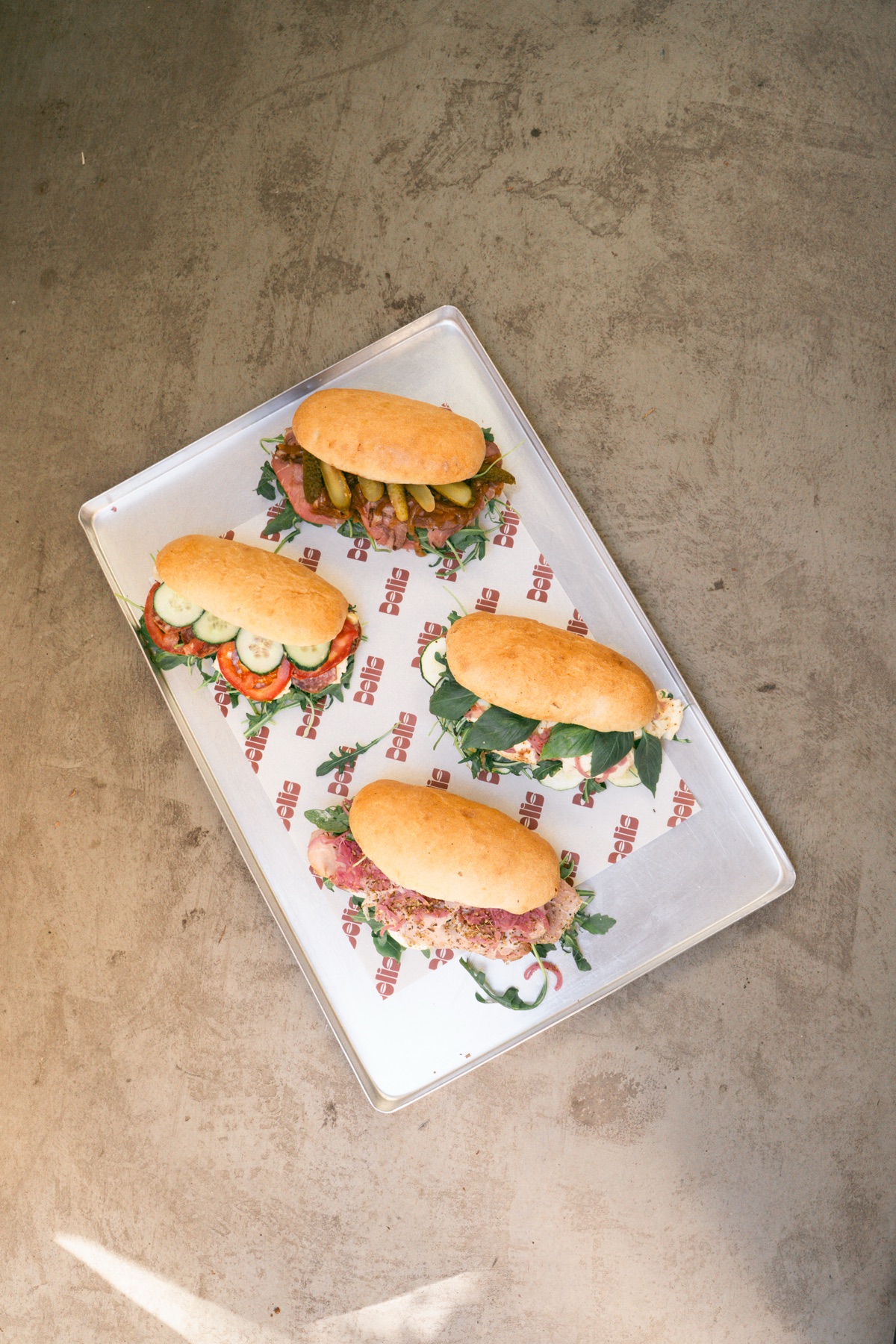 Four sandwiches on a tray with DELIS paper, shot from above on concrete