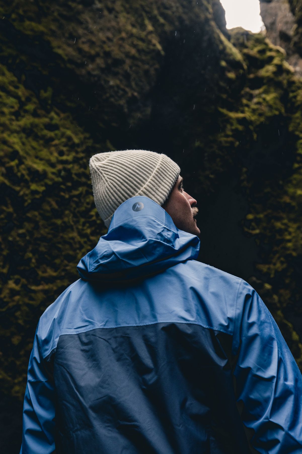 Hiker in a blue Marmot shell looking up at a mossy gorge