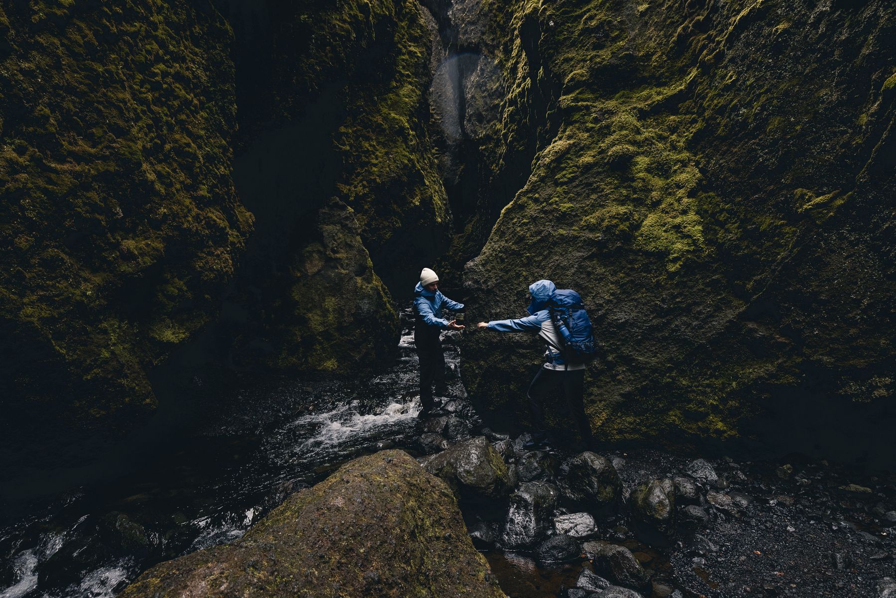 Two hikers helping each other across a stream in a gorge
