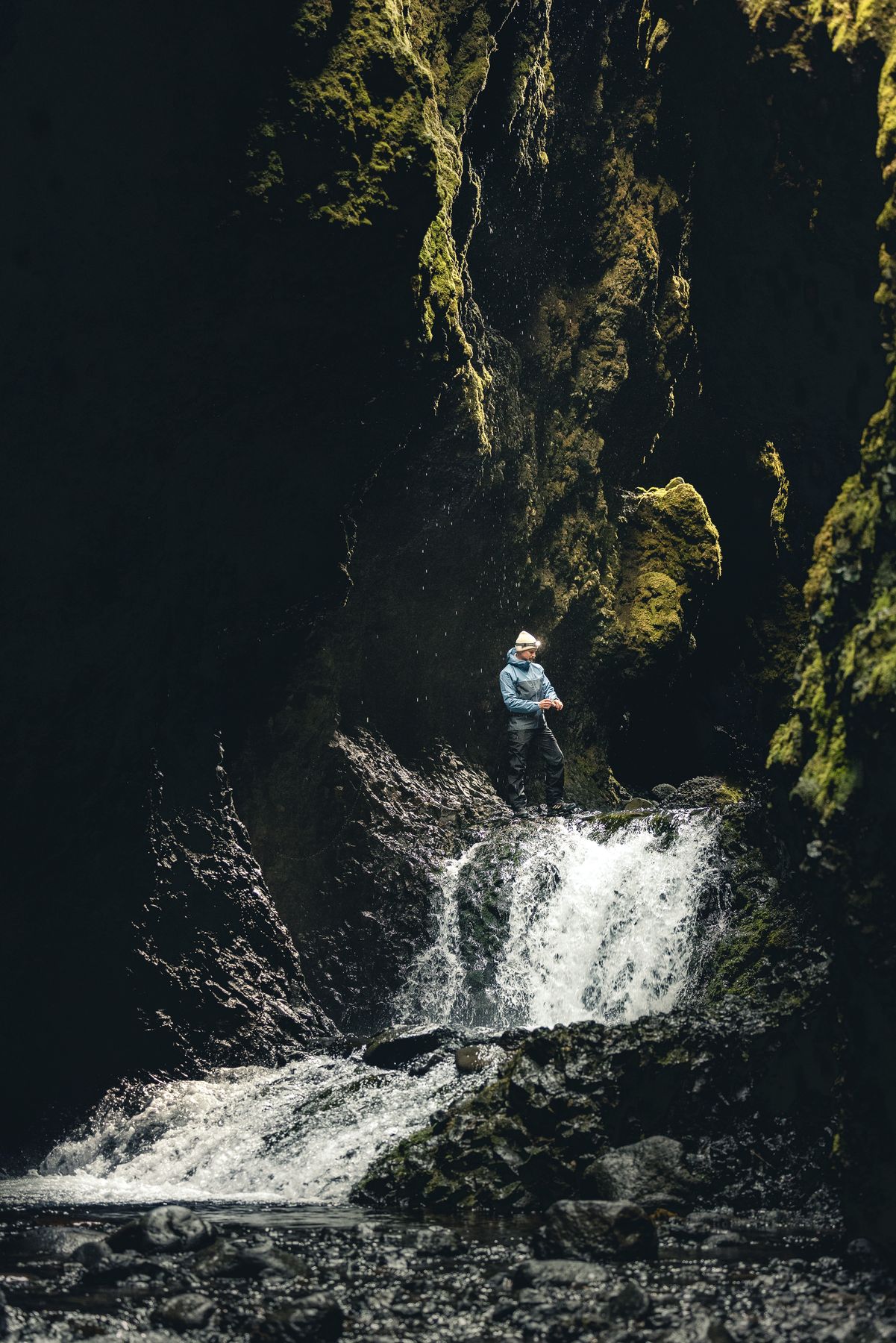Hiker standing above a small waterfall in a dark canyon