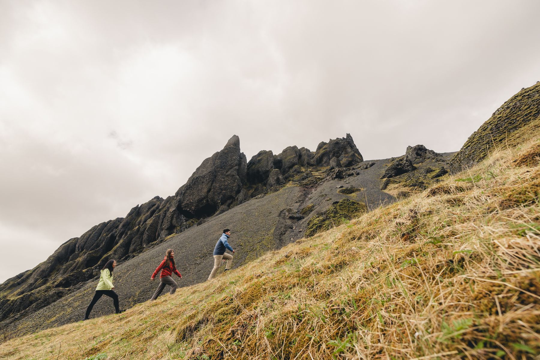 Three hikers climbing a grassy slope under rock towers
