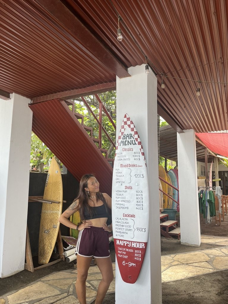 Finished surfboard sign with the happy hour menu, leaning against a column at the hostel